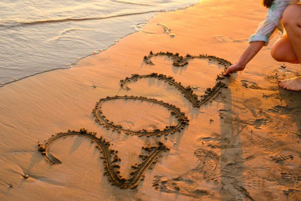 A woman on a beach draws 2023 into the sand