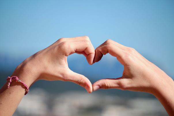 Two hands form a heart in front of blue sky