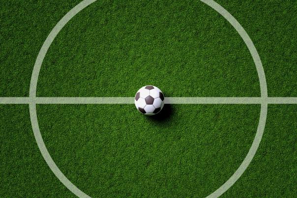 A soccer ball sits at the center circle on a soccer pitch.
