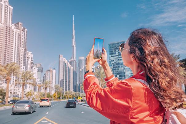 A woman using her phone to take a picture of a tall skyscraper.