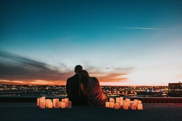 A couple leans into each other while surrounded by candles to look at a city skyline from a hill