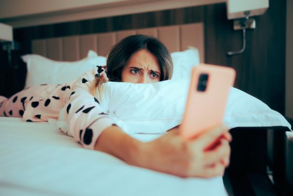 A person laying face down on a bed, staring at their phone, with a concerned look on their face.