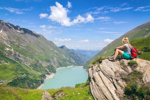 A hiker overlooks a pristine mountain lake, reflecting the regenerative tourism focus on restoring and protecting natural landscapes.