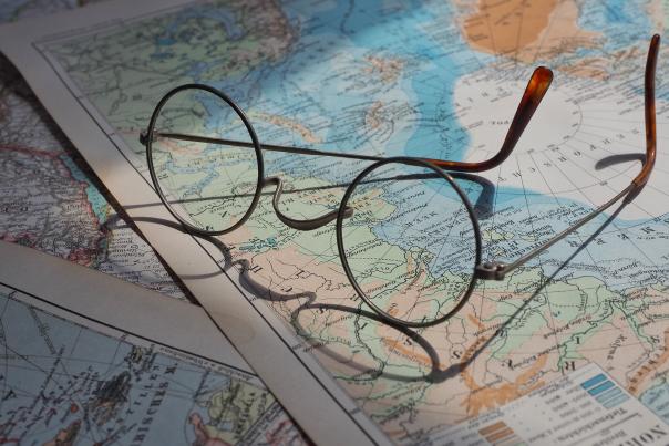 Eyeglasses rest on a table on top of physical maps of the world.
