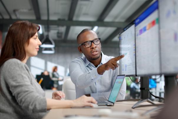 Two professionals review CRM dashboard data on dual monitors during a meeting sales strategy session, illustrating practical CRM tactics and best practices for improving sales team performance and adoption.