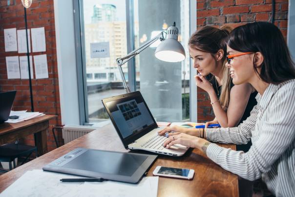Two people leaning over a desk, looking intently at a laptop containing website design files.