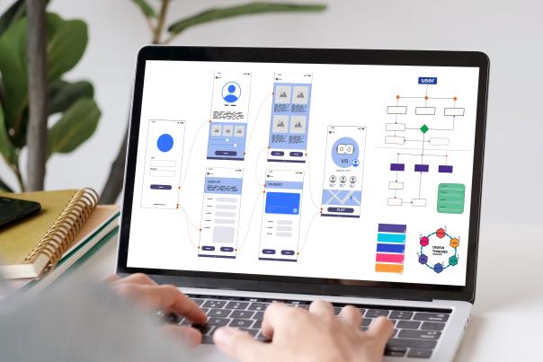 Laptop screen showing a website design workflow with wireframes, UI elements, and navigation flowcharts.