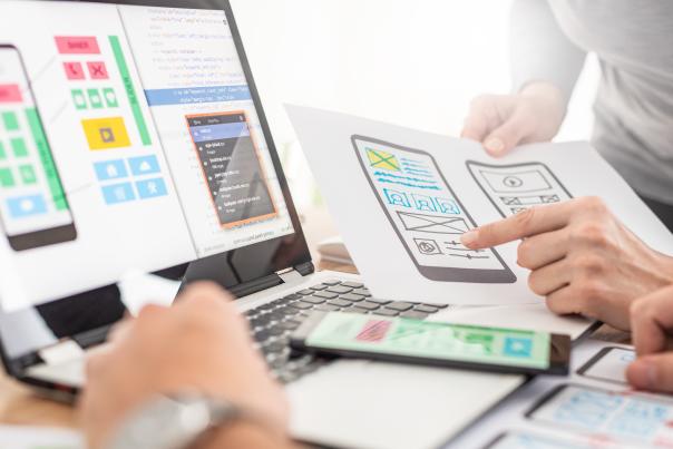 Designers reviewing mobile-first wireframes and prototypes on paper and a laptop screen.