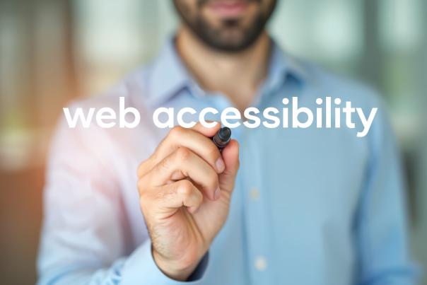 Close-up of a person writing the words “web accessibility” on a transparent surface, representing the importance of prioritizing accessible digital experiences.