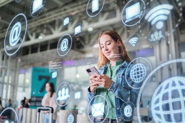 Traveler using a smartphone in a transit hub, surrounded by digital communication and connectivity icons representing smart travel technology.