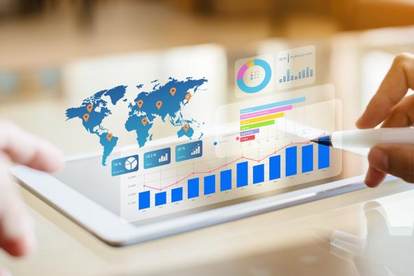 Hands using a stylus on a tablet displaying global map markers and layered data charts, illustrating how destination marketers analyze and track tourism trends.