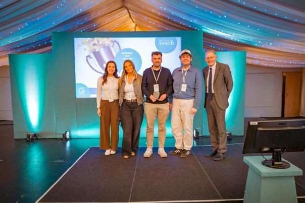 Team of five onstage receiving the Destination Team of the Year award at an awards event, standing in front of a trophy-themed presentation screen.