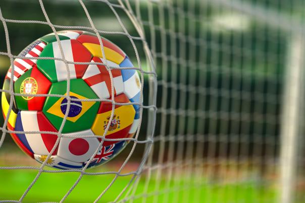 A soccer ball with the flags of countries from around the world, hits the net of a goal.