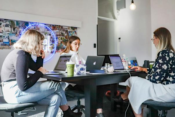 Three women work on their laptops while seated at the same table.