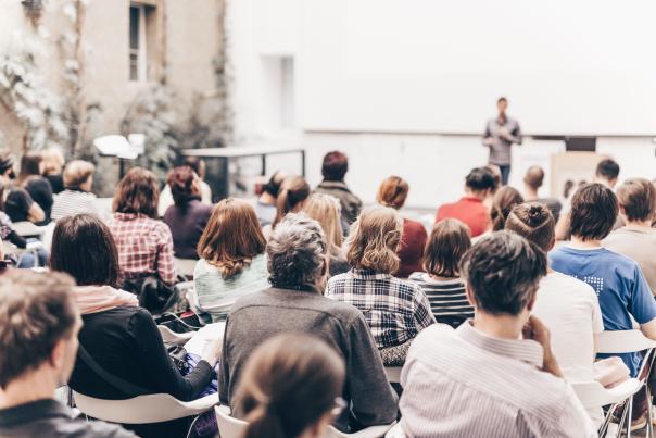 A person giving a presentation as people sit closely in a small meeting room.