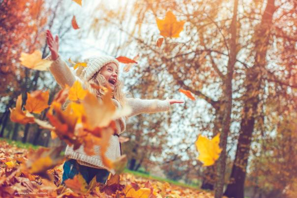 Older woman joyfully throwing leaves in autumn