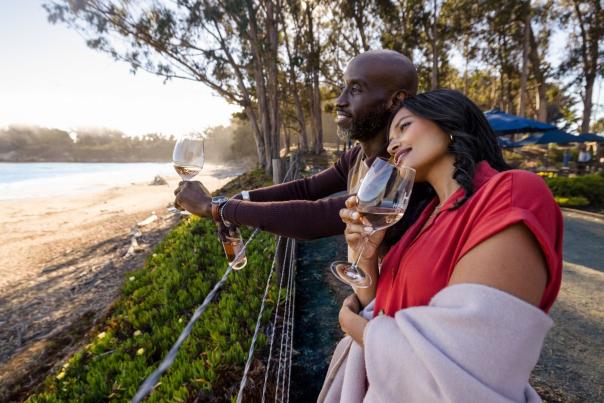 Couple looking out at the ocean holding glasses of wine