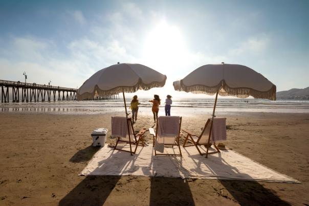 Beach chairs and umbrellas set up on the sand with women running towards the water in the background