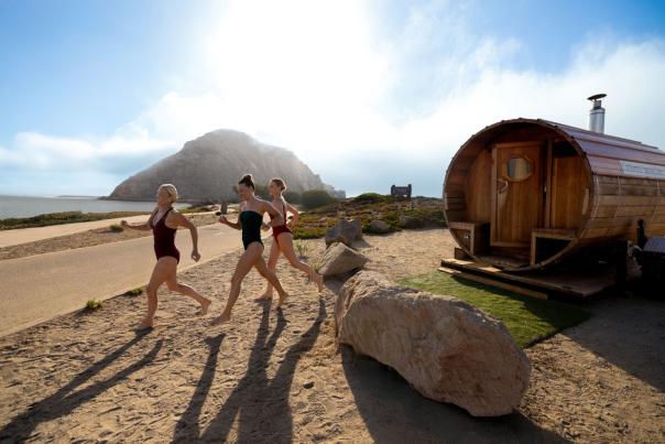 Three women running from the sauna to the bay with Morro Rock in the background