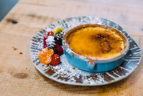 Creme brulee with fresh berries and powdered sugar garnish on a rustic wooden table.