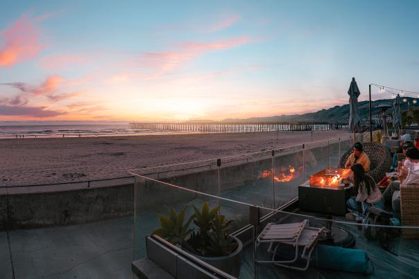 People watching sunset on a patio overlooking the beach with a firepit