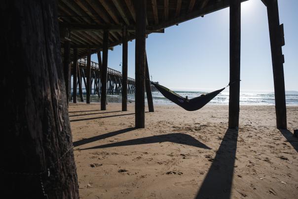 Person reading in a hammock under a pier next to the ocean