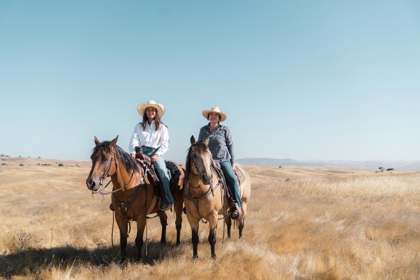 Two women on horseback with cowboy hats on Camatta Ranch among golden grass