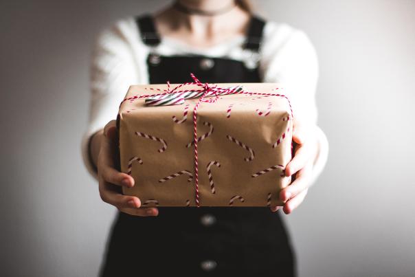Person in soft focus holding out a wrapped present to the camera