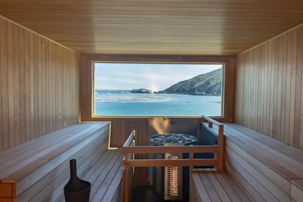 Interior view of a wood sauna with view out the window of the ocean and hill