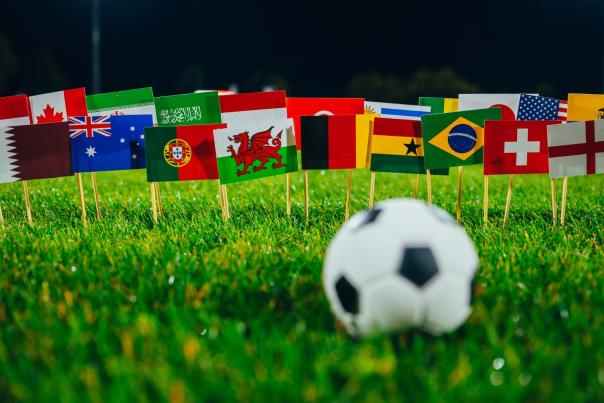 Football on grassy field in front of collection of flags of the world including England, Wales, Portugal, Germany and more