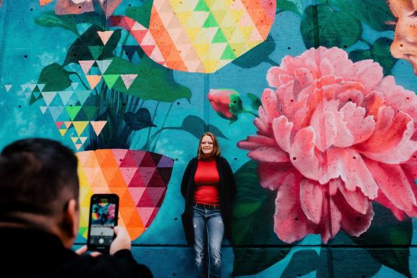 man taking picture of woman in front of mural