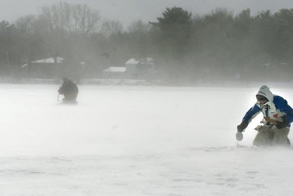 photo of two people ice fishing and placing a tip-ups in a blizzard