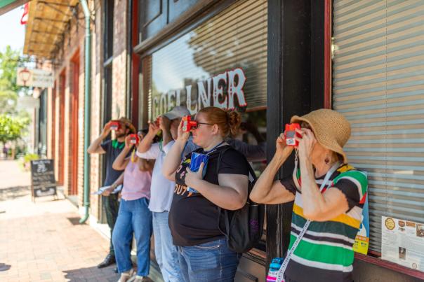 A group of people looking through ViewMasters on a Hit the Bricks walking tour on Historic Main Street in St. Charles, Missouri.