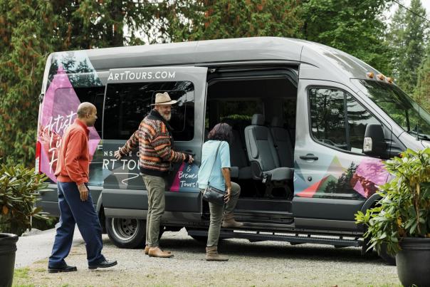 A man holds a van door open while people climb in.