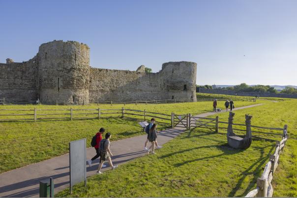 A group walk towards the gates at Pevensey Castle, with the turrets in view