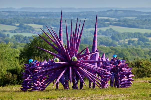 A giant spiky purple creature with yellow eyes in a field
