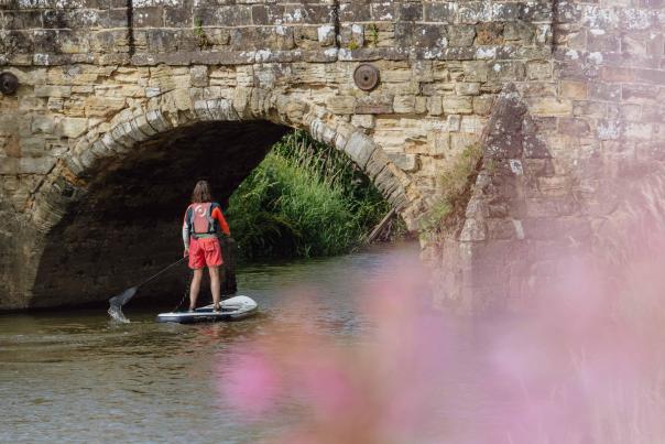 Paddleboarder under bridge on river