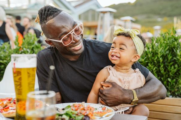 Smiling father holding a baby daughter enjoying a meal outside