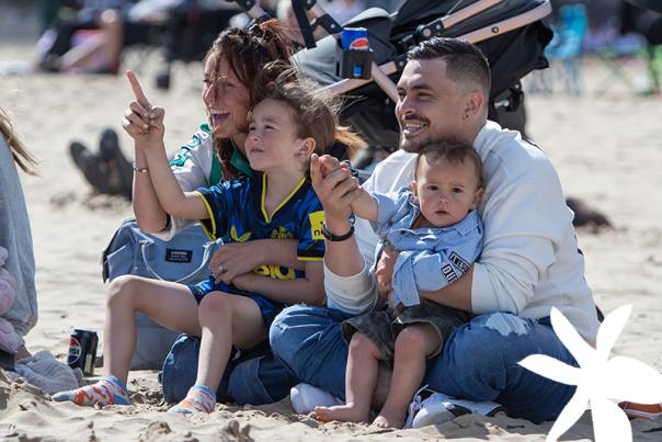 A woman, man and two small children sitting on the beach pointing at the sky.