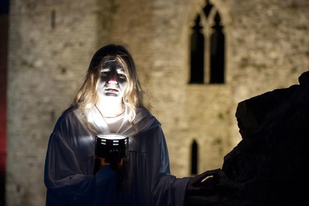 Creepy woman holding a torch under her chin outside Oystermouth Castle