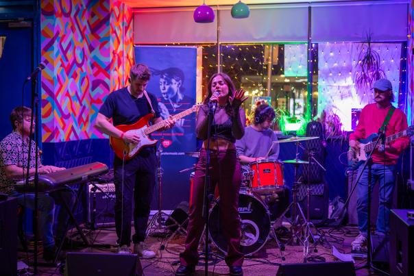 A young five piece band with female singer playing on a colourful stage.