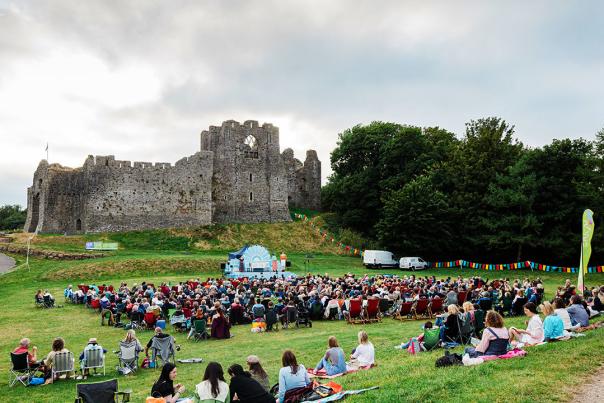 Crowds watching an outdoor theatre show with Oystermouth Castle in the background