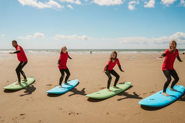 A family of four standing on surf boards on the sand practicing moves.