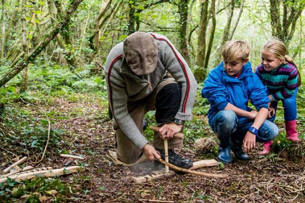 A man teaching two children how to start a fire using sticks