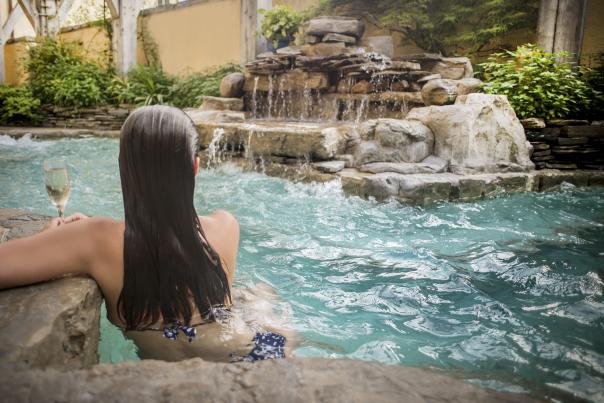 Woman lounging in hot tub around rock formation with glass of wine
