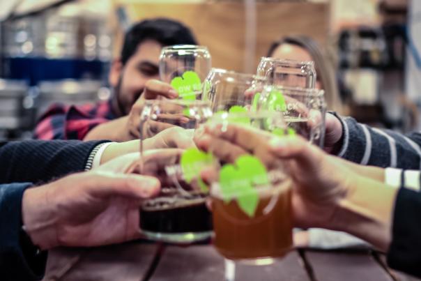 4 sets of hands and arms coming together for a cheers of transparent beer glasses with green leaf logos