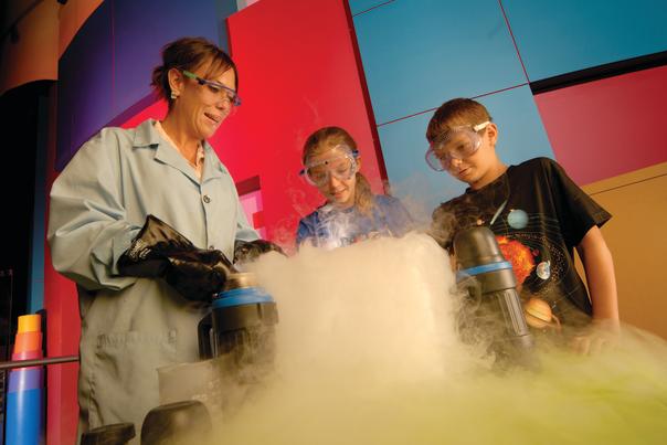 Woman Wearing Goggles Shows Two Young Kids an Experiment at the Museum of Science and Technology with Smoke