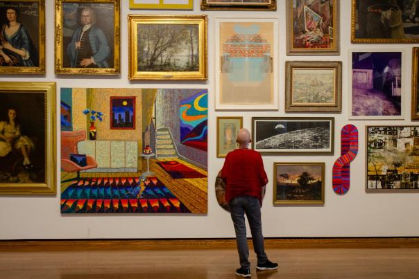 A person in a red sweater looking up at a wall filled with art