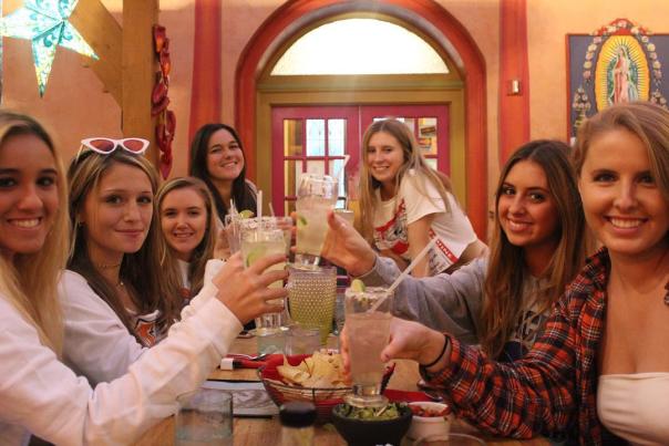 Group of young girls cheering drinks over a table while smiling at the camera in a restaurant