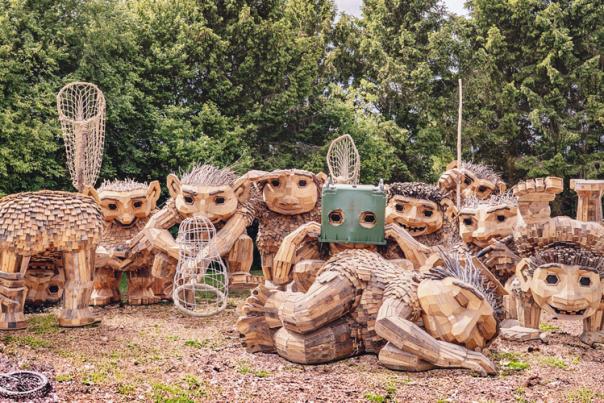 Twelve reclaimed-wood troll sculptures from Thomas Dambo’s TROLLS: A Field Study gathered outdoors.